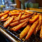 A close-up shot of perfectly roasted carrots, glistening and seasoned, arranged on a wire rack.