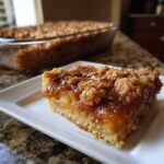 A mouthwatering slice of Apple Snickerdoodle Dump Cake on a white plate, showcasing a gooey apple filling and crumb topping.