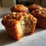 Close-up of a delicious banana nut muffin with a bite taken out, topped with chopped walnuts.