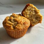 Close-up of two banana protein muffins, one whole and one broken in half to show the moist interior.