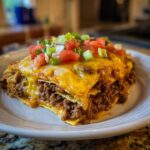 A mouthwatering slice of beef taco casserole topped with melted cheese, tomatoes, and green onions.