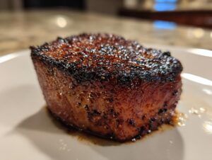A perfectly cooked Blackened Tuna Steak on a white plate, showcasing its dark, seasoned crust and moist interior.