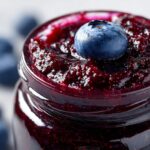 Close-up of a jar filled with glistening homemade blueberry jam, topped with a fresh blueberry.