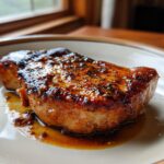 A close-up of a perfectly cooked brown sugar garlic pork chop glistening in its own juices on a plate.
