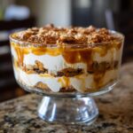A beautiful caramel cookie trifle layered with cream, cookies, and drizzled caramel sauce in a glass trifle dish.