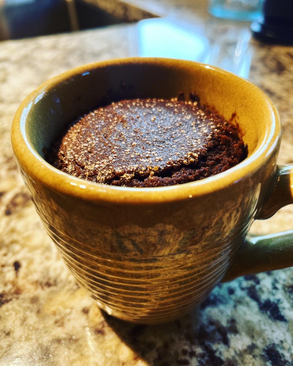 Close-up of a rich chocolate protein mug cake, dusted with powdered sugar, in a rustic mug.