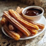 A plate of golden brown churros dusted with sugar, served with a bowl of rich chocolate dipping sauce.