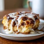 A close-up of a decadent slice of cinnamon roll casserole drizzled with sweet icing.