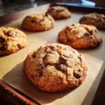 Close-up of freshly baked classic chocolate chip cookies on a baking sheet, with visible chocolate chunks.