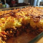 A close-up of a freshly baked Classic Shepherd's Pie in a glass dish, showing a golden-brown mashed potato topping over a rich meat filling.