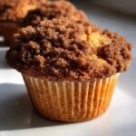 Close-up of a tall, domed coffee cake muffin topped with a generous cinnamon streusel.