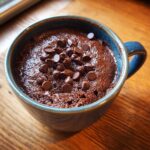A delicious Cottage Cheese Microwave Brownie topped with melted chocolate chips in a blue mug.