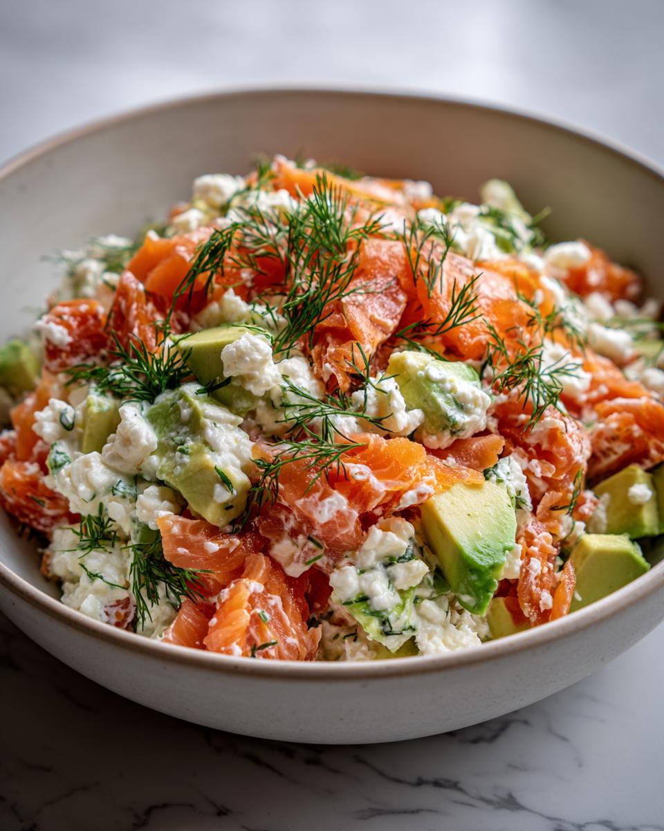 A close-up of cottage cheese smoked salmon salad with chunks of avocado and fresh dill in a white bowl.