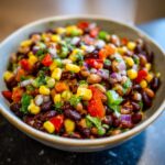 A close-up of a bowl filled with vibrant Cowboy Caviar, featuring black beans, corn, red bell peppers, and red onion.
