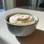 A close-up of a bowl filled with creamy garlic aioli, showing its smooth texture and speckled surface.