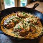 Four juicy creamy garlic parmesan pork chops simmered in a rich sauce and garnished with parsley in a cast iron skillet.