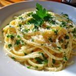 A close-up of a white plate filled with creamy lemon pasta, topped with fresh parsley and grated cheese.