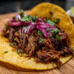 A close-up of a delicious crock pot shredded beef taco, topped with red onions and cilantro.
