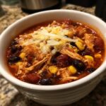 A bowl of hearty Crockpot Chicken Enchilada Soup topped with shredded cheese, black beans, and corn.