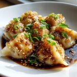 Close-up of dumplings coated in a rich, glossy dumpling sauce, sprinkled with sesame seeds and green onions.