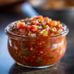 Close-up of a glass jar filled with vibrant fresh tomato canned salsa, showing diced tomatoes, onions, peppers, and cilantro.