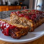 A slice of moist garlic butter turkey meatloaf topped with ketchup glaze and herbs.