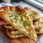 A hand holding a slice of fluffy garlic naan bread, topped with melted butter, garlic, and fresh parsley.