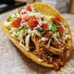 A close-up of a delicious Healthy Crockpot Chicken Tacos in a crispy shell, topped with shredded lettuce, tomatoes, and cheese.