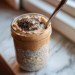 Close-up of high protein overnight oats in a jar, topped with peanut butter and chia seeds, with a spoon.