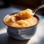A spoonful of warm, chunky homemade applesauce being lifted from a rustic blue bowl.