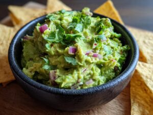 Close-up of a bowl of fresh Homemade Guacamole, topped with cilantro and red onion, with tortilla chips in the background.