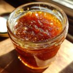 A close-up of a glass jar filled with glistening honey BBQ sauce, showing its rich amber color and texture.