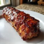 A close-up of a perfectly cooked maple mustard pork tenderloin with a glossy glaze on a white plate.