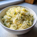 A close-up of fluffy Mediterranean lemon rice in a white bowl, garnished with fresh parsley and lemon zest.