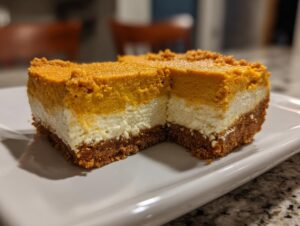 A close-up of a layered no bake pumpkin cheesecake slice on a white plate, showing the graham cracker crust, cream cheese layer, and pumpkin topping.