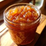 Close-up of a glass jar filled with glistening, chunky old-fashioned pear preserves.