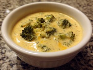 A close-up of a white bowl filled with creamy Panera Broccoli Cheddar Soup, featuring tender broccoli florets.
