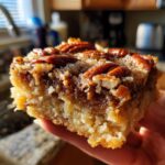 A close-up of a moist slice of pecan pie dump cake, topped with whole pecans and a glistening glaze.