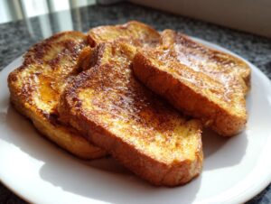 Close-up of golden-brown protein french toast slices drizzled with syrup on a white plate.
