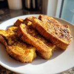 A plate piled high with golden-brown slices of protein french toast, dusted with cinnamon.