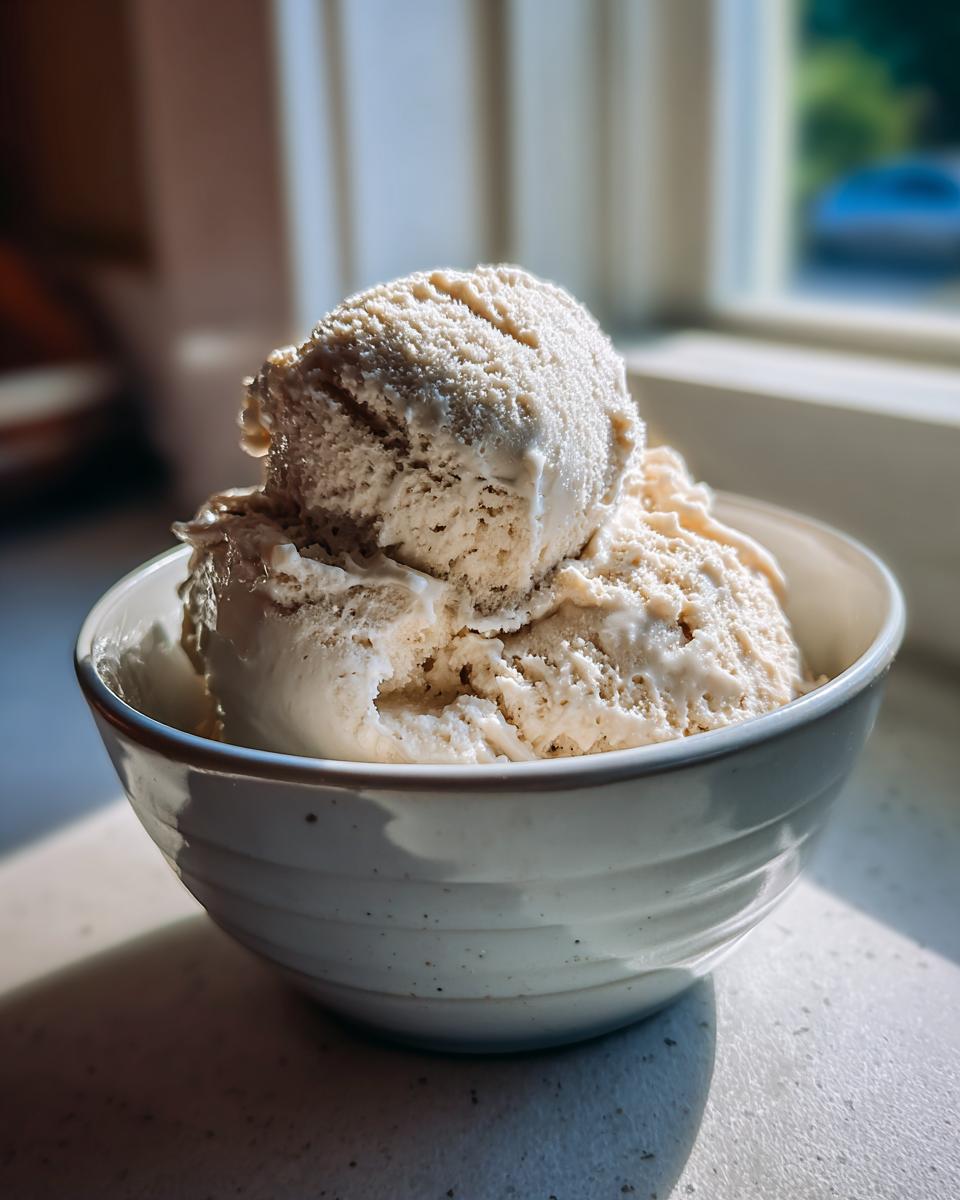 Close-up of two scoops of creamy protein ice cream in a white bowl, bathed in sunlight.