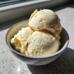 Close-up of three scoops of creamy vanilla protein ice cream in a light blue bowl.