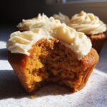 A close-up of a delicious pumpkin spice cupcake with a bite taken out, revealing its moist texture and topped with creamy frosting.