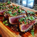 Close-up of perfectly seared ahi tuna slices, coated in sesame seeds and herbs, served in a rich sauce.