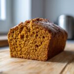 A close-up of a freshly baked sourdough pumpkin bread loaf on a wooden cutting board, showing its moist crumb.