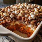A close-up of a baked sweet potato casserole topped with toasted marshmallows and a crumble topping.
