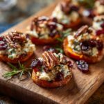 Close-up of sweet potato rounds topped with goat cheese, dried cranberries, and pecans on a wooden board.