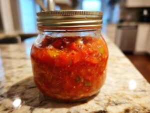 A close-up of a glass jar filled with vibrant, chunky tomato salsa, ready for canning.