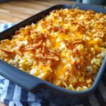A close-up of a baked Tuna Casserole in a grey baking dish, topped with melted cheddar cheese and crunchy cornflakes.