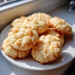 A pile of golden brown whipped shortbread cookies on a white plate, bathed in sunlight.